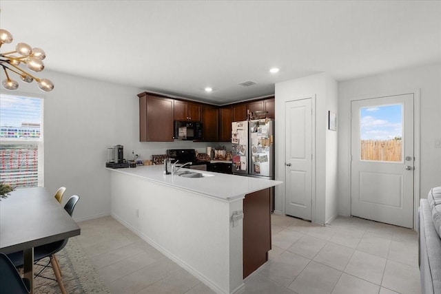 kitchen with freestanding refrigerator, a peninsula, light countertops, dark brown cabinets, and black microwave