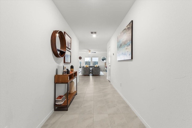 hallway with light tile patterned flooring, visible vents, and baseboards