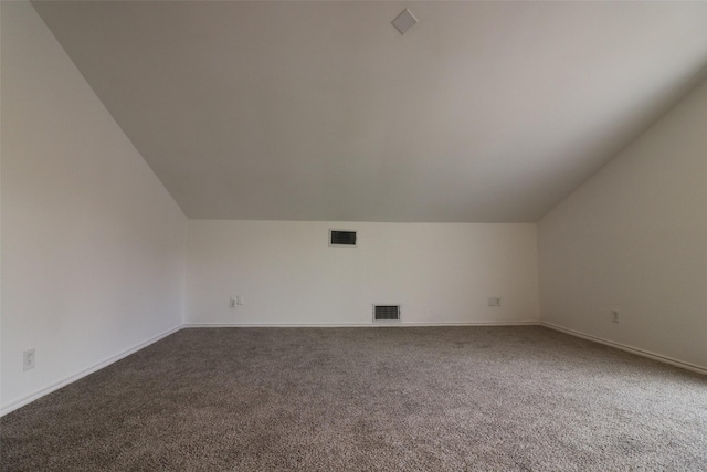 additional living space featuring lofted ceiling, dark carpet, and visible vents