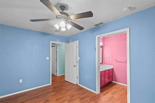 unfurnished bedroom with ceiling fan, ensuite bathroom, light wood-style flooring, visible vents, and baseboards