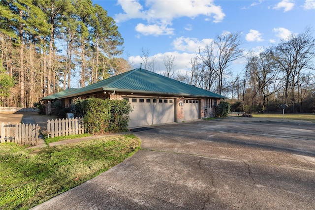 view of home's exterior with driveway, a garage, metal roof, fence, and brick siding