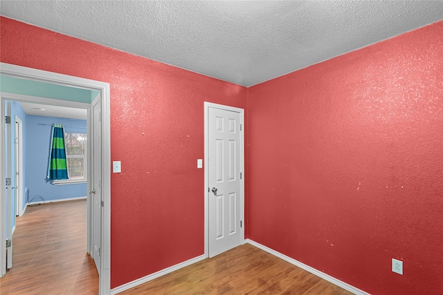 spare room with a textured ceiling, a textured wall, wood finished floors, and baseboards