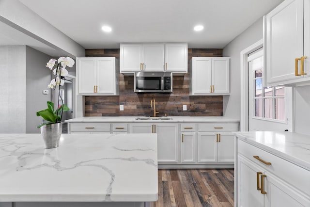 kitchen featuring light stone counters, stainless steel microwave, white cabinets, and a sink