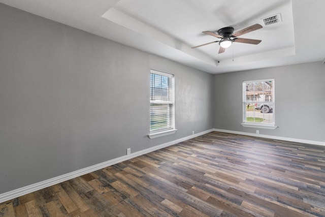 empty room with dark wood-type flooring, a tray ceiling, visible vents, and baseboards