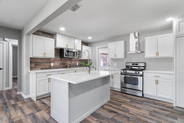 kitchen with wall chimney exhaust hood, white cabinetry, stainless steel appliances, and a center island