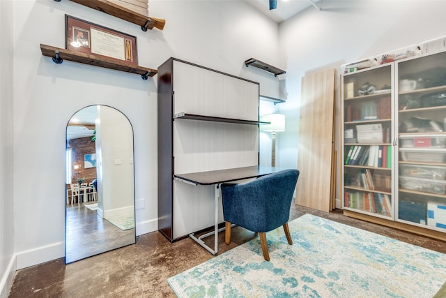 office area with concrete flooring, a towering ceiling, and baseboards