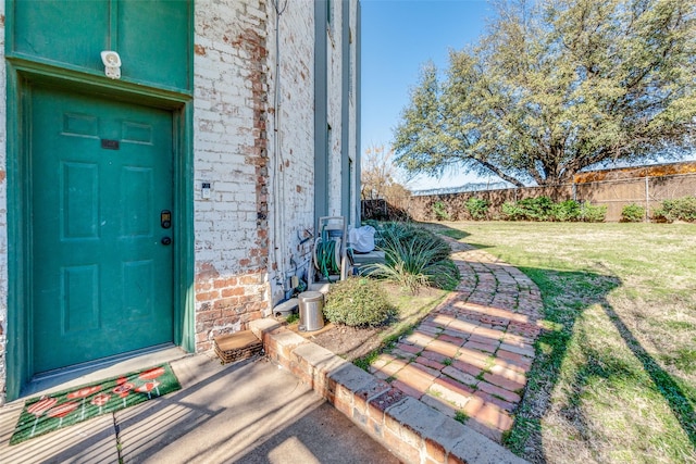 view of exterior entry with a yard, brick siding, and fence