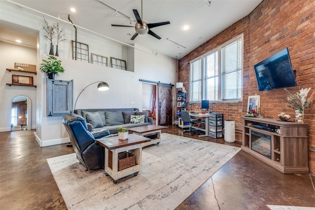 living room featuring a barn door, a high ceiling, brick wall, baseboards, and concrete flooring