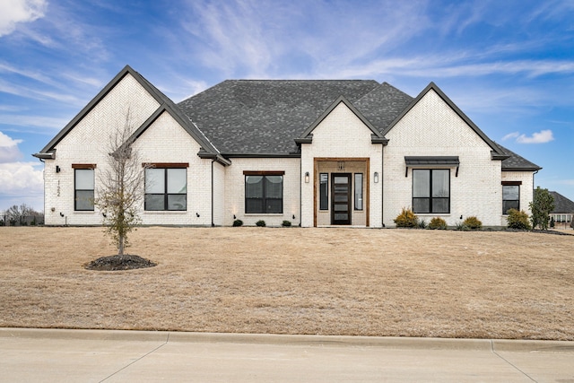 view of front of house featuring brick siding, a front yard, and a shingled roof