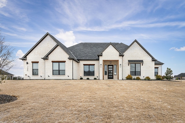 view of front facade with roof with shingles, brick siding, and a front lawn