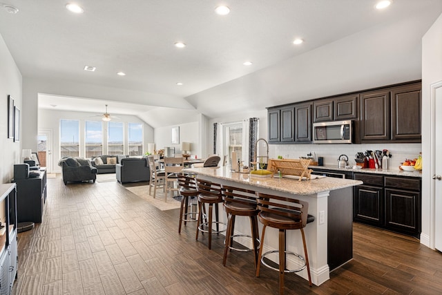 kitchen featuring open floor plan, stainless steel microwave, a breakfast bar area, and a kitchen island with sink