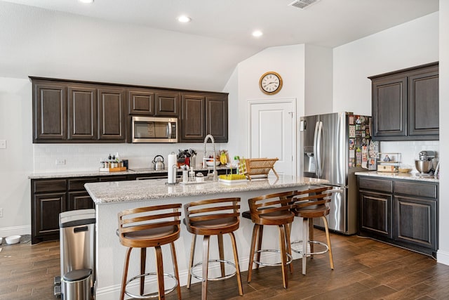 kitchen with vaulted ceiling, a center island with sink, stainless steel appliances, and dark wood-style flooring