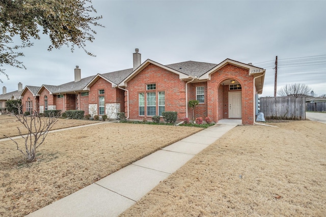 view of front of property featuring brick siding, fence, a front lawn, and roof with shingles