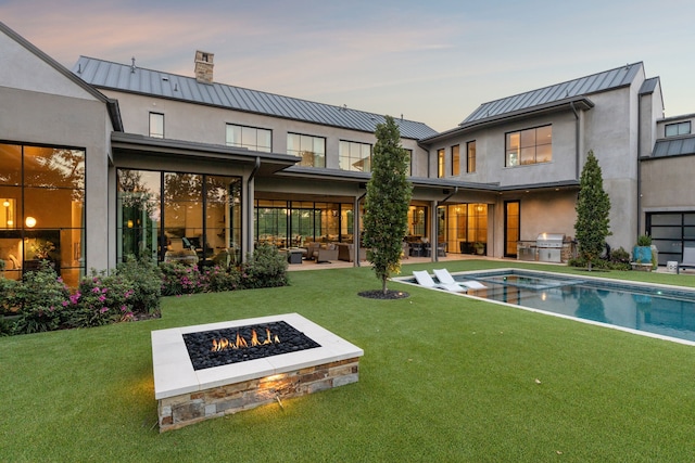 back of property featuring a yard, an outdoor fire pit, a standing seam roof, and area for grilling