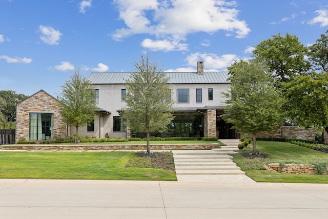 view of front of house featuring stone siding, a front lawn, a standing seam roof, and stucco siding