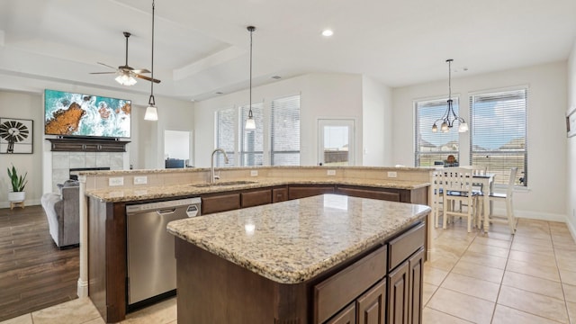 kitchen with light stone counters, a center island, decorative light fixtures, stainless steel dishwasher, and a sink