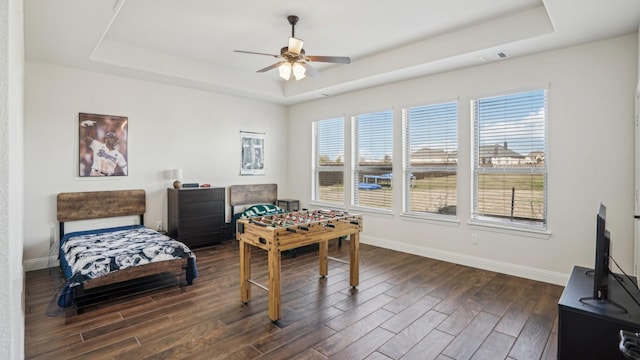 rec room with dark wood-style floors, ceiling fan, a tray ceiling, and baseboards