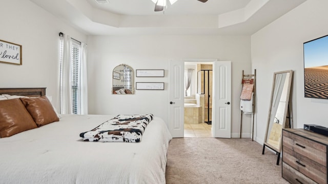 bedroom with a tray ceiling, light carpet, connected bathroom, and ceiling fan