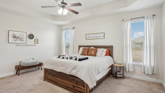 bedroom with baseboards, a tray ceiling, a ceiling fan, and light colored carpet