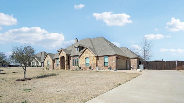 french country home featuring a garage, brick siding, fence, concrete driveway, and a chimney