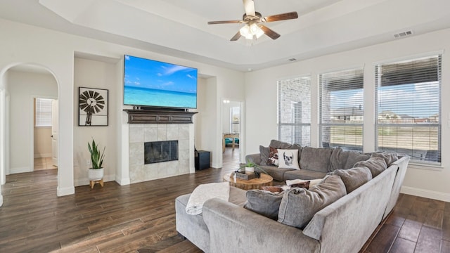 living room with dark wood-style floors, arched walkways, a raised ceiling, and a tile fireplace