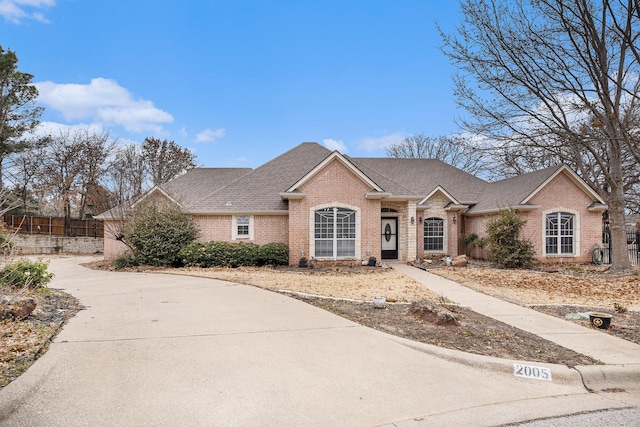 view of front of property with a shingled roof, brick siding, and fence