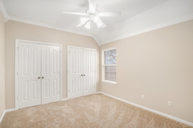 unfurnished bedroom featuring multiple closets, light colored carpet, crown molding, and baseboards