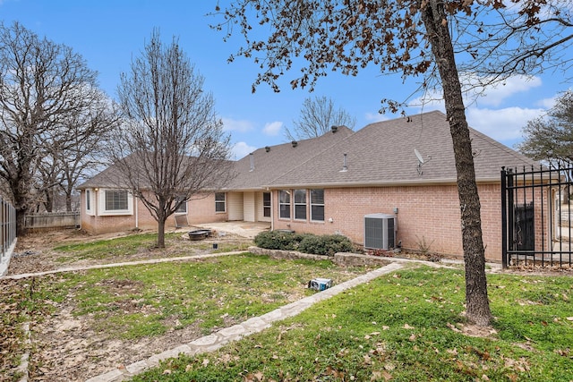 back of property with an outdoor fire pit, a lawn, fence, cooling unit, and brick siding