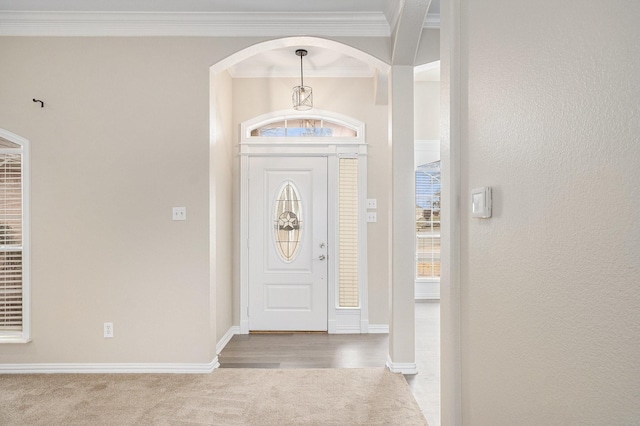 entryway featuring baseboards, light carpet, arched walkways, and crown molding