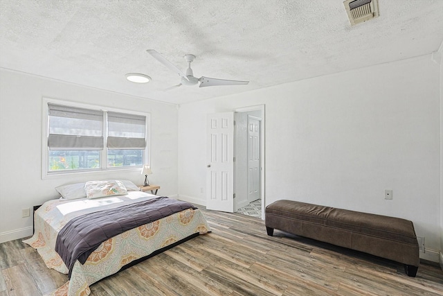 bedroom featuring visible vents, ceiling fan, a textured ceiling, wood finished floors, and baseboards