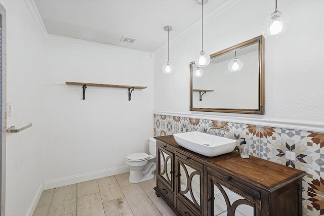 half bathroom with visible vents, wainscoting, toilet, ornamental molding, and wood finished floors