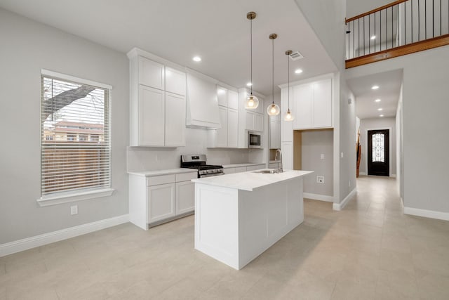 kitchen featuring a center island with sink, custom range hood, appliances with stainless steel finishes, white cabinetry, and a sink