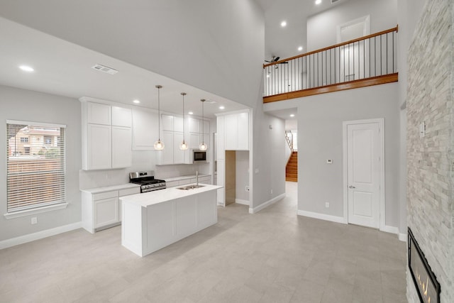 kitchen featuring stainless steel appliances, a sink, white cabinets, a center island with sink, and pendant lighting