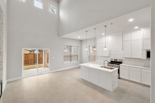 kitchen with white cabinetry, light countertops, hanging light fixtures, stainless steel range with gas cooktop, and an island with sink