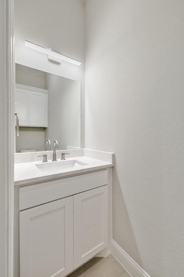 bathroom with a textured wall, vanity, baseboards, and tile patterned floors