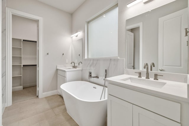 bathroom with a soaking tub, two vanities, a walk in closet, and a sink