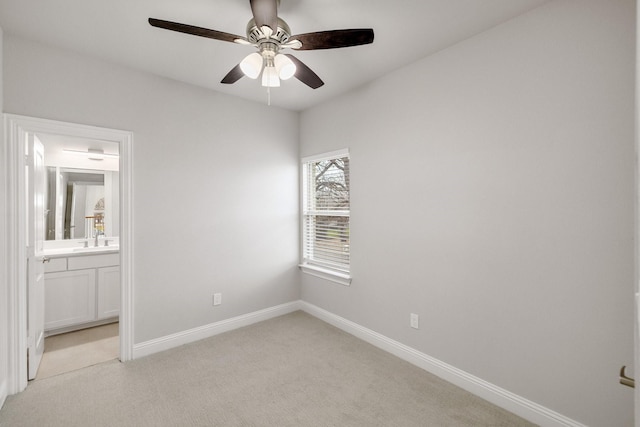 unfurnished bedroom featuring ensuite bathroom, a ceiling fan, light carpet, a sink, and baseboards