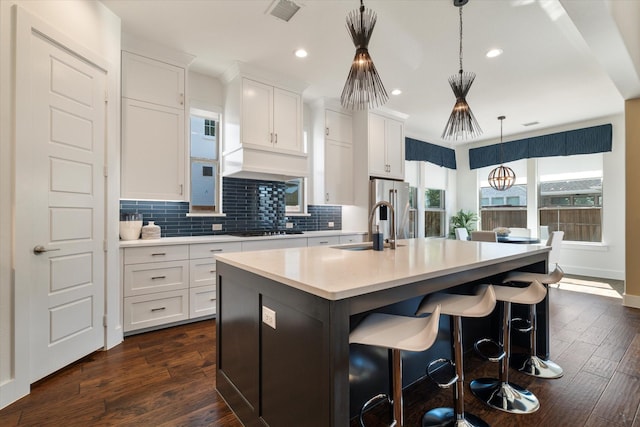 kitchen featuring white cabinets, an island with sink, hanging light fixtures, light countertops, and a sink