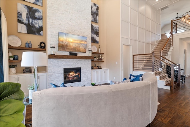 living room featuring dark wood-style floors, built in features, a fireplace, a high ceiling, and stairs