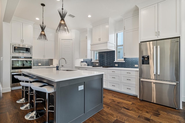 kitchen featuring stainless steel appliances, white cabinetry, hanging light fixtures, light countertops, and an island with sink