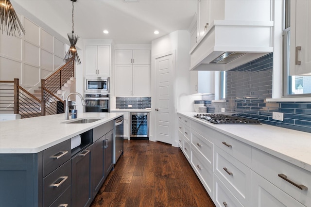 kitchen with pendant lighting, beverage cooler, stainless steel appliances, white cabinets, and custom range hood