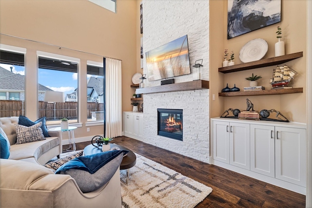 living room with a towering ceiling, a fireplace, baseboards, and dark wood finished floors