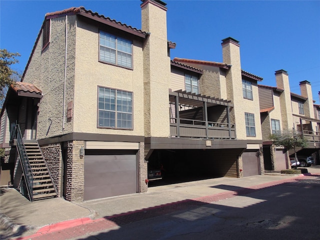 exterior space featuring an attached garage, a chimney, stairway, and stucco siding