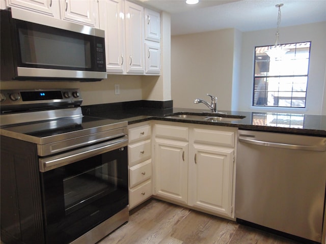 kitchen featuring dark stone counters, a sink, stainless steel appliances, white cabinets, and light wood-type flooring