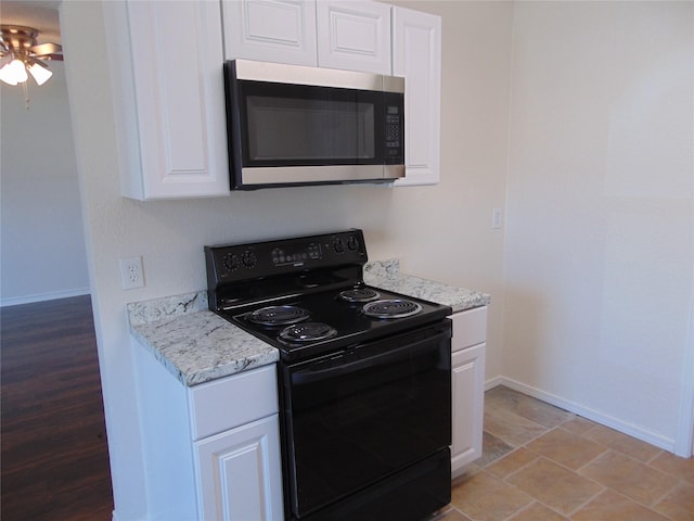 kitchen with black range with electric cooktop, stainless steel microwave, light stone countertops, and white cabinetry