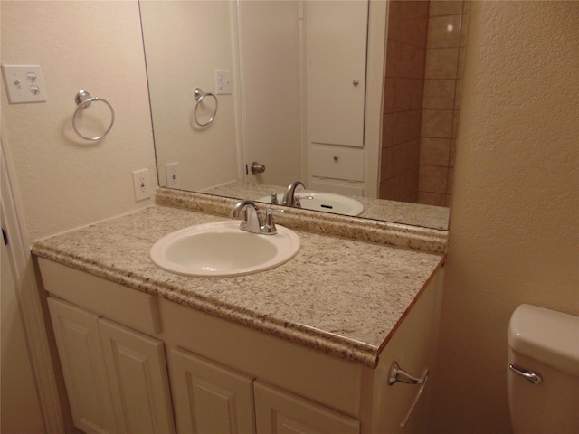 bathroom with a textured wall, vanity, and toilet