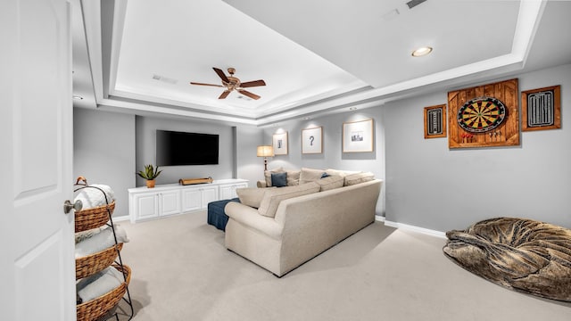 living area with baseboards, a raised ceiling, a ceiling fan, and light colored carpet