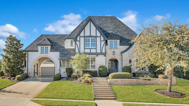 english style home with a shingled roof, a front lawn, a gate, and stucco siding