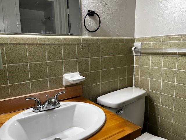 bathroom with toilet, vanity, tile walls, and a textured wall