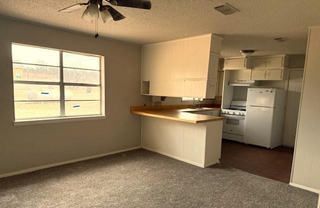 kitchen featuring a textured ceiling, a peninsula, white appliances, a ceiling fan, and dark carpet